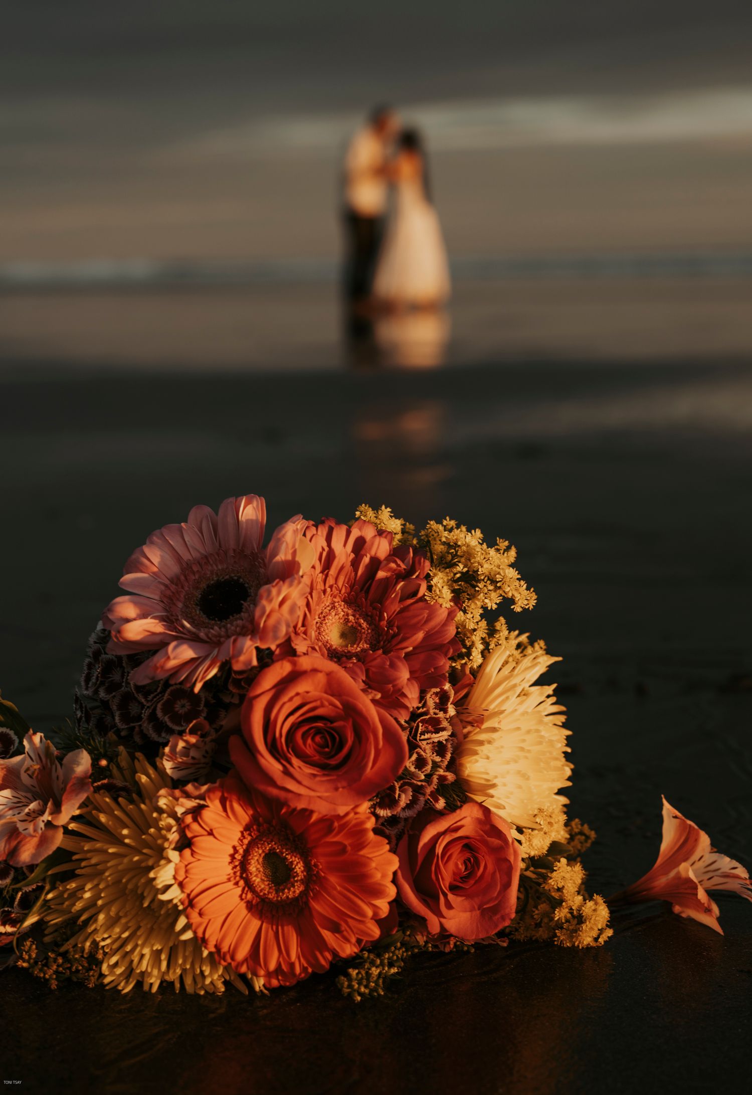 A romantic sunset silhouettes a couple in water while orange and yellow flowers bloom in the foreground.