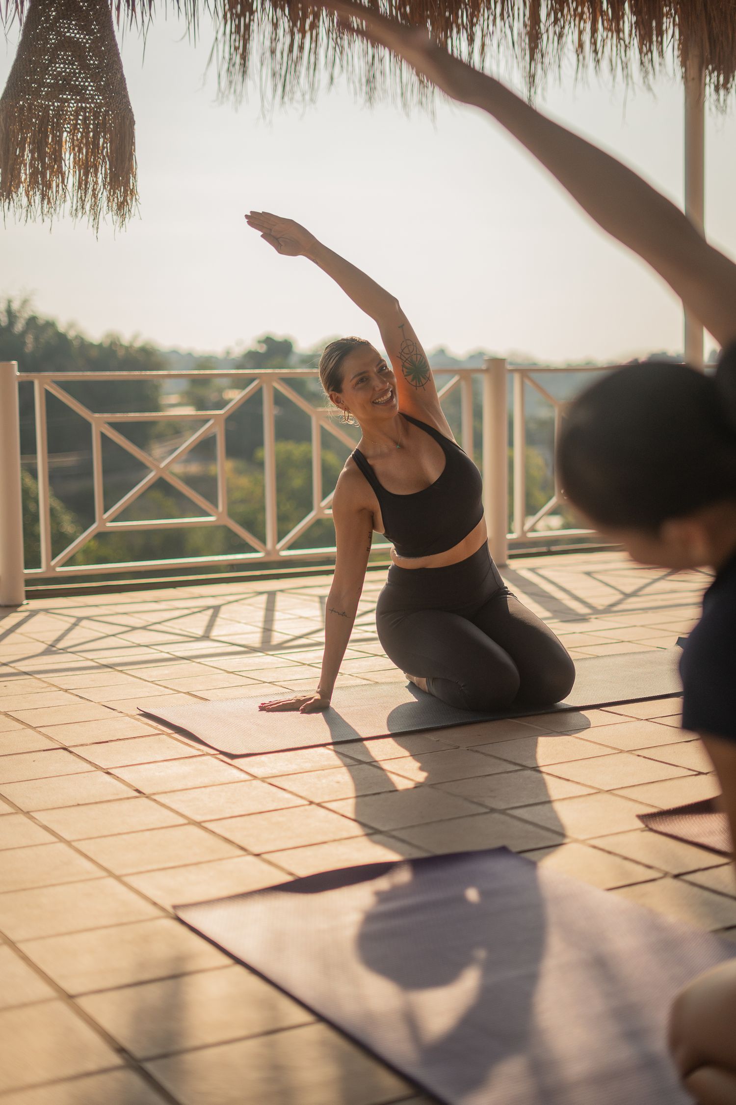 A yoga practitioner performs a side bend stretch on a mat during a beachfront session at sunset.
