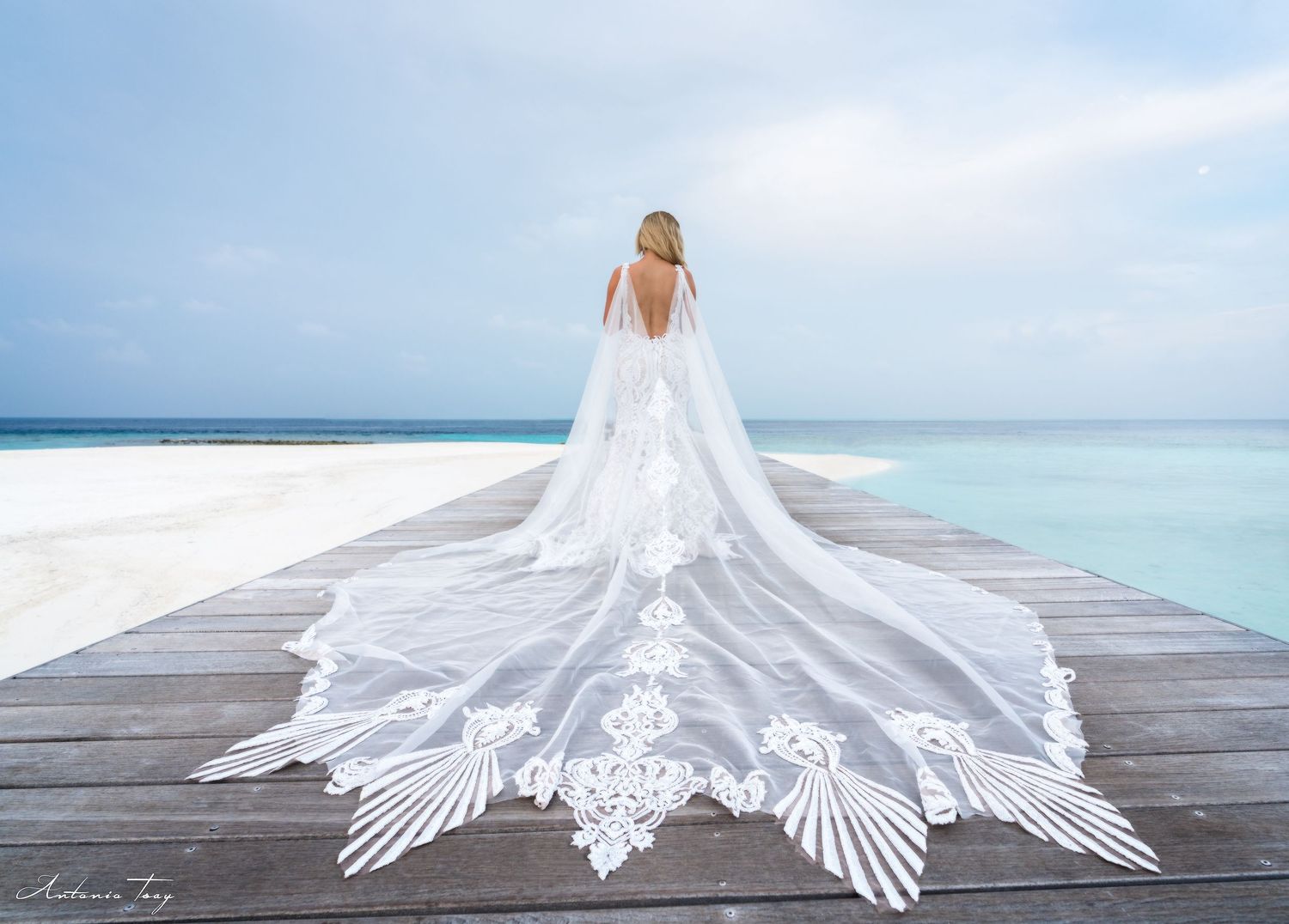 White wedding dress train laid out symmetrically on wooden dock over turquoise waters. Maldives.