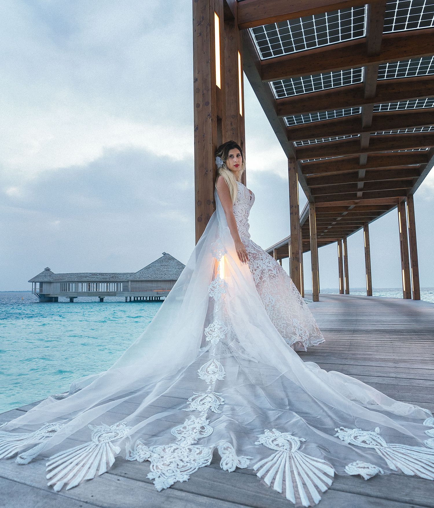 Stunning wedding dress with intricate lace train photographed on overwater villa boardwalk in tropical paradise.