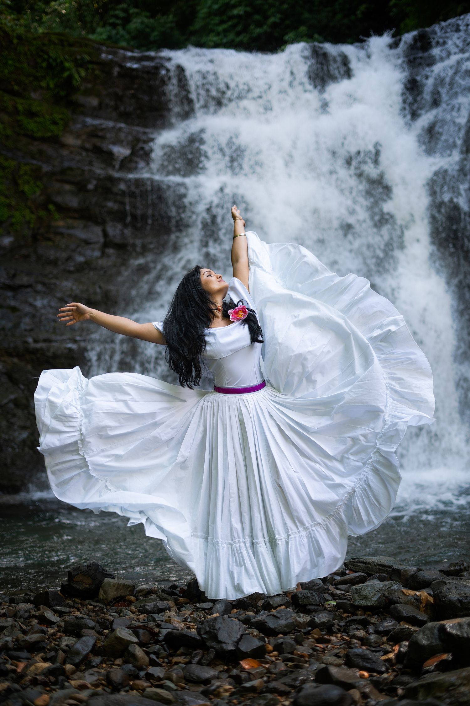 Person in flowing white dress dancing dramatically in front of cascading waterfall. Manuel Antonio, Costa Rica.