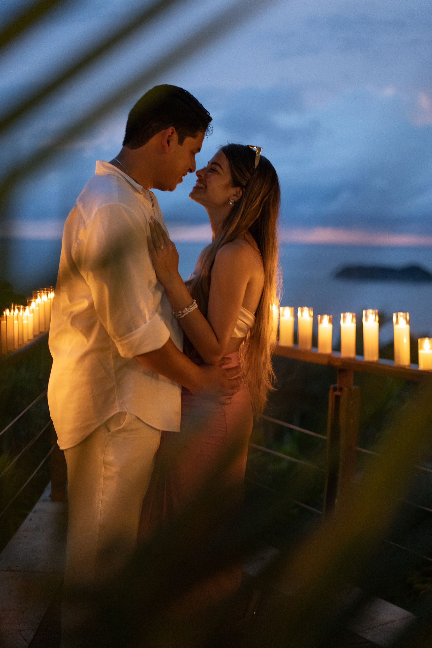 Romantic couple sharing intimate moments at sunset with candlelit walkway along the beach.