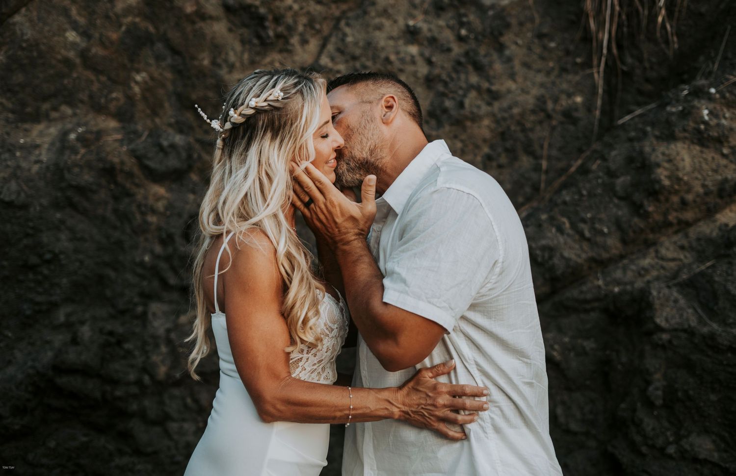 A romantic couple shares intimate moments in a series of black and white photos against a dark stone wall background.