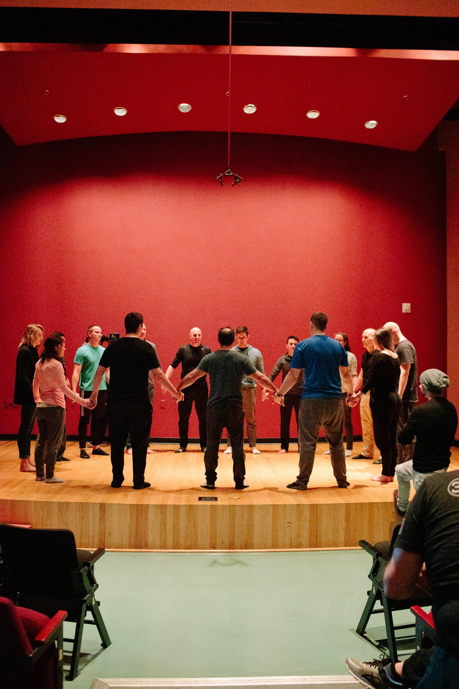 Group activity session on wooden stage with red backdrop and audience seating.