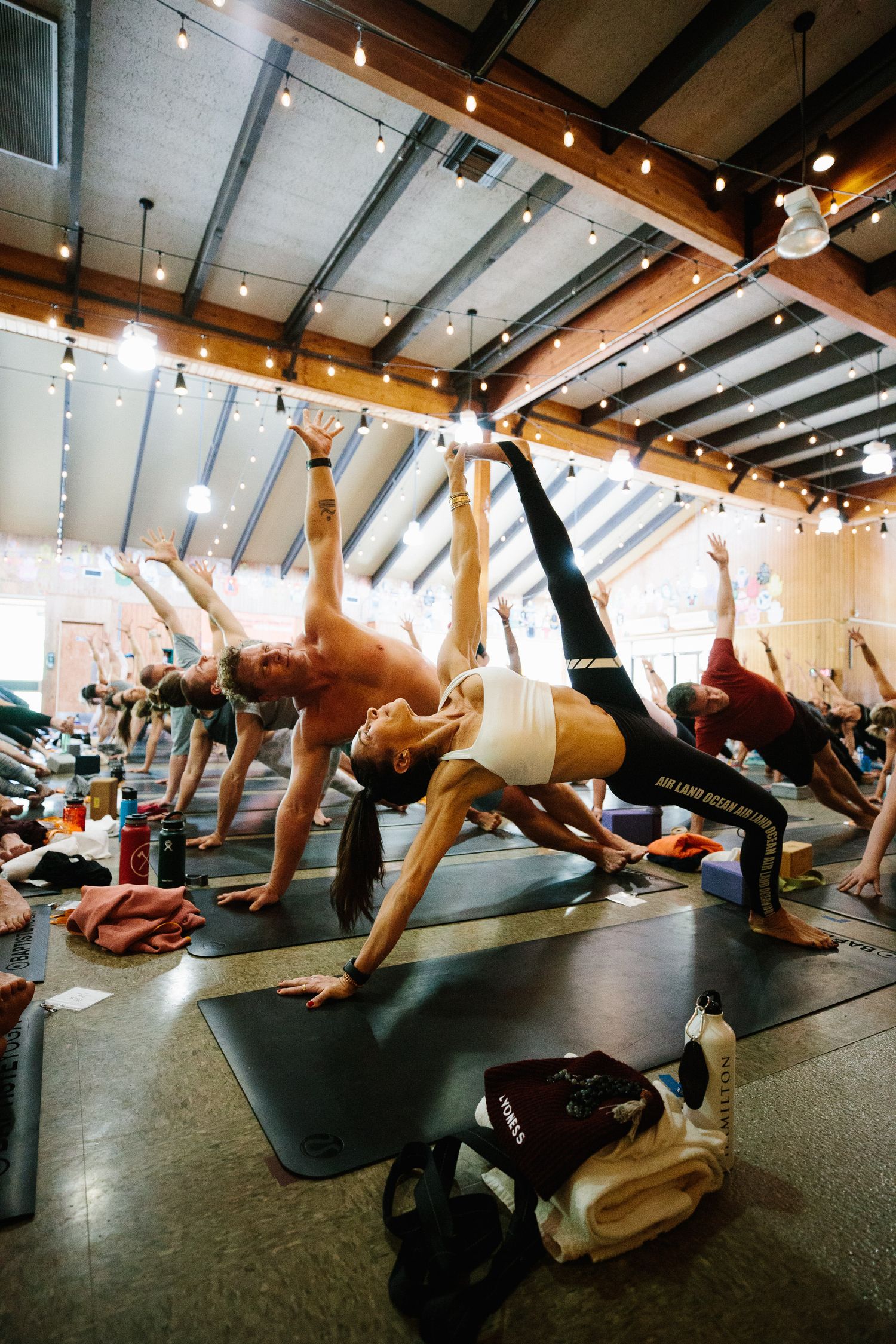 Large group performs aerial exercises on suspended straps in an indoor fitness studio.