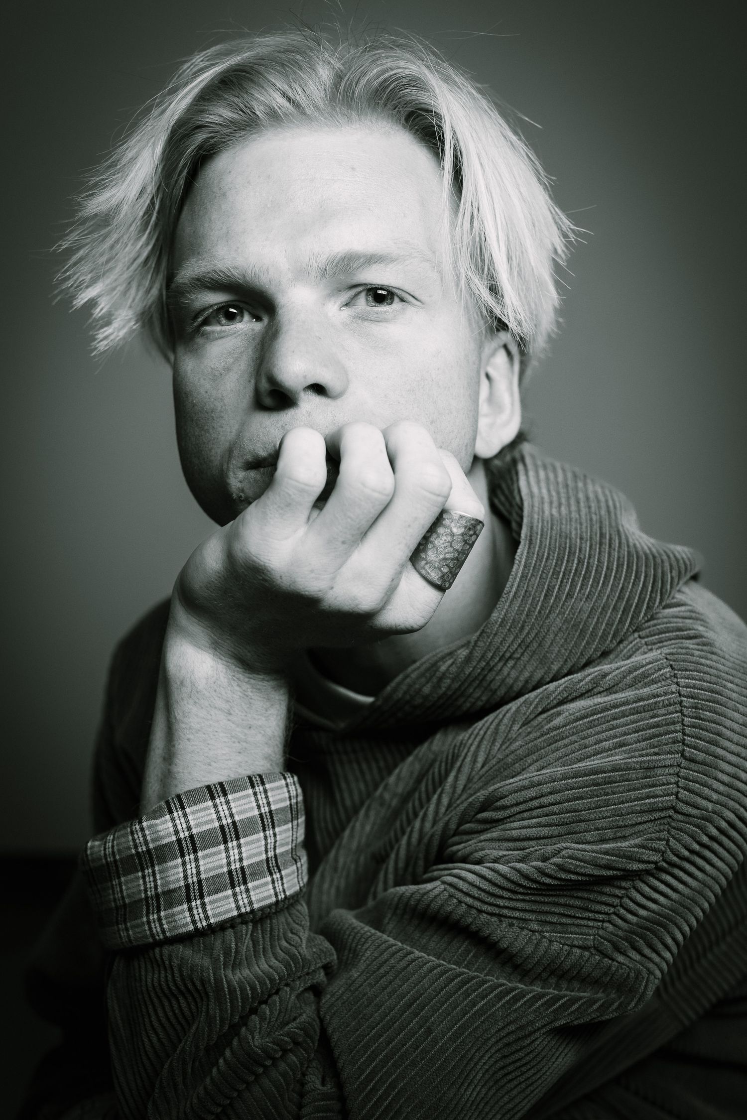 Black and white photo of a contemplative young man with platinum hair resting hand on face.