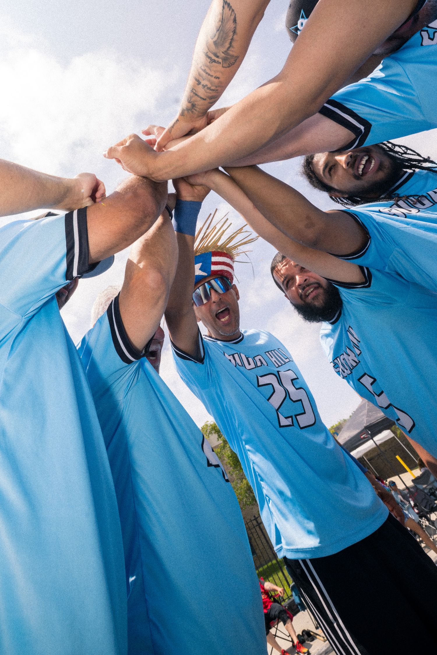Low angle view of basketball teammates in light blue jerseys joining hands together in a huddle formation.