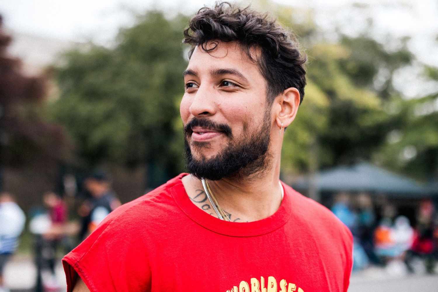 Person in red t-shirt smiling outdoors at sporting event.