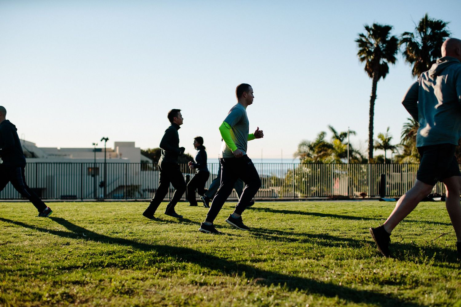 Silhouettes of people running and exercising on grass during sunrise or sunset.