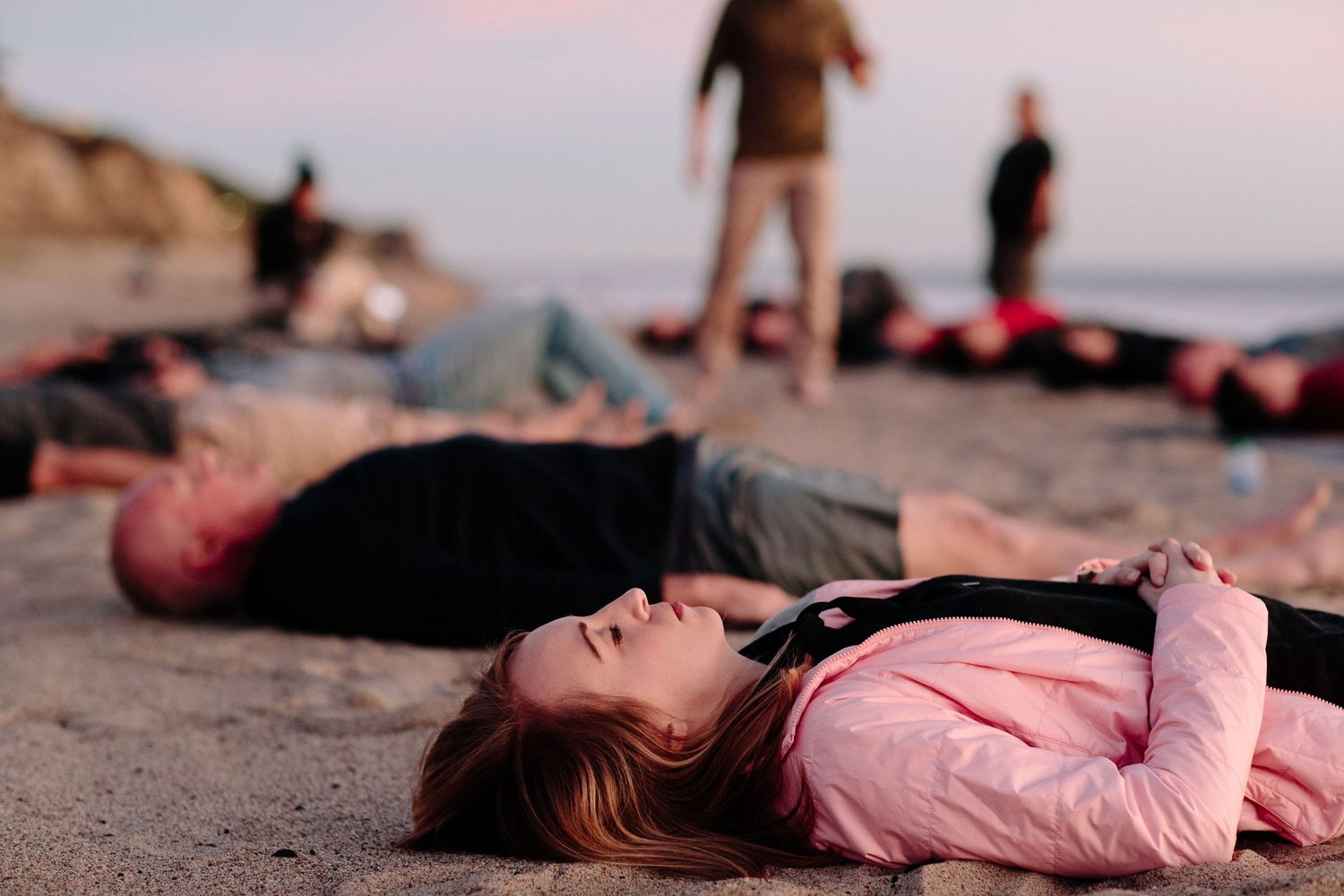 People lying on beach sand at sunset creating artistic poses.