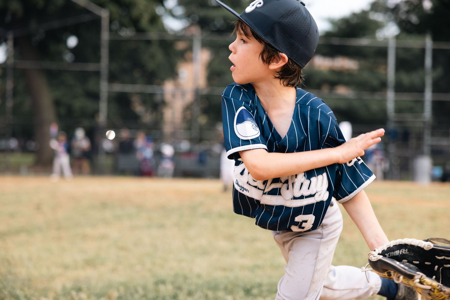 Young baseball player in navy pinstripe uniform follows through on pitching motion during practice on grass field.