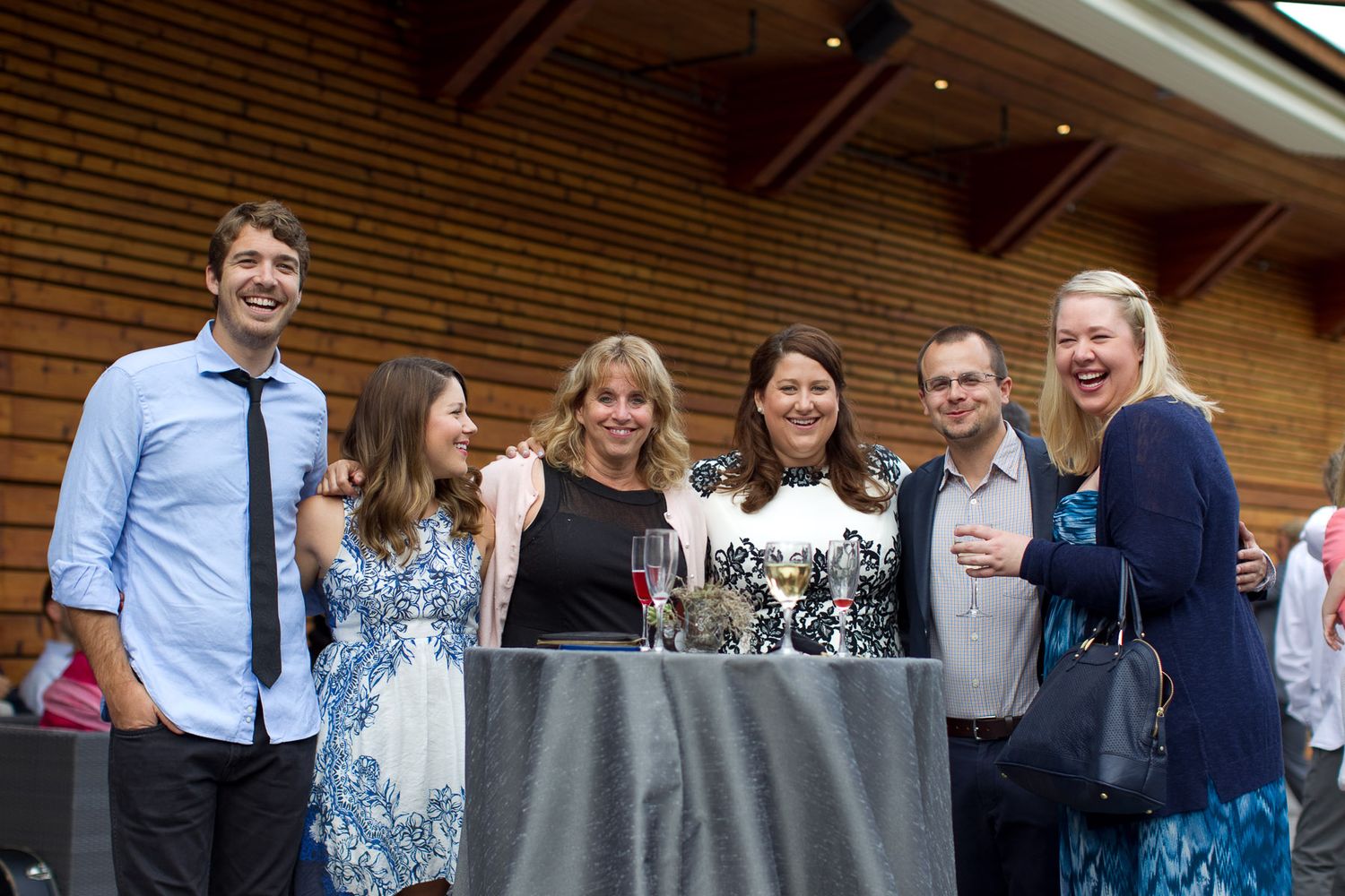 Friends gathered around a table at an outdoor event sharing drinks and smiles.