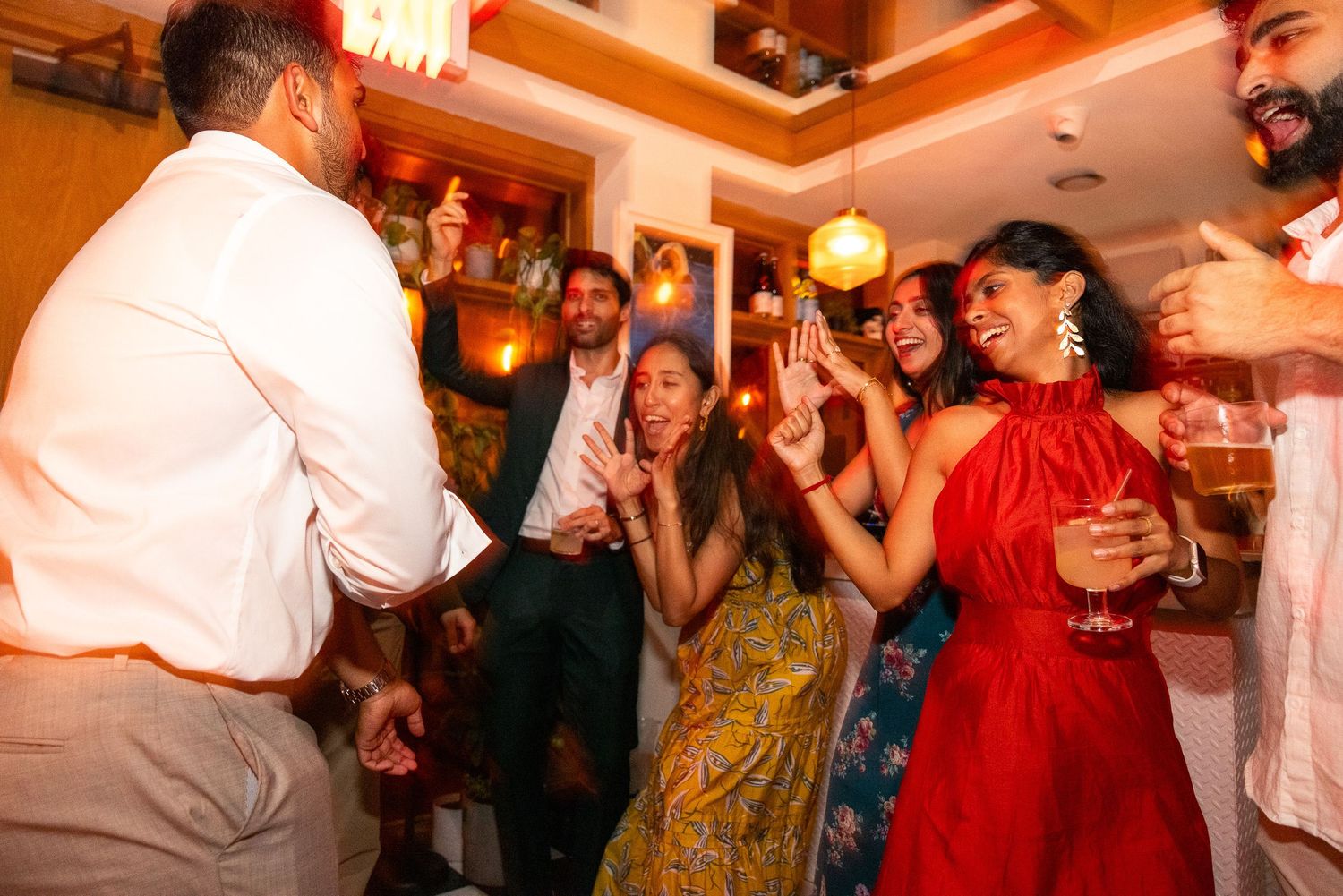 Guests dance and socialize at a lively indoor reception with warm lighting.
