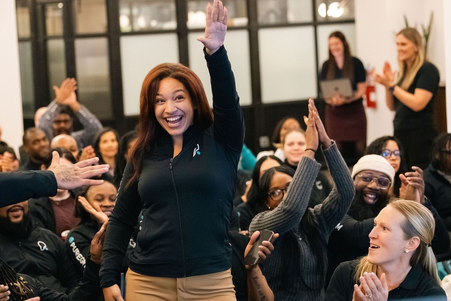 Business professionals participate in an engaging workshop session with raised hands and animated expressions.