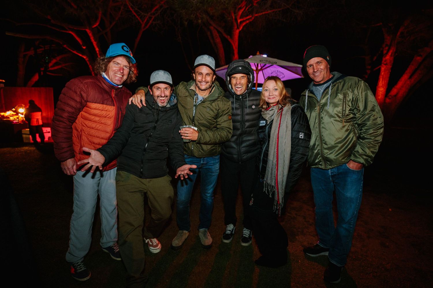 Group gathering at night with red atmospheric lighting in an outdoor setting.