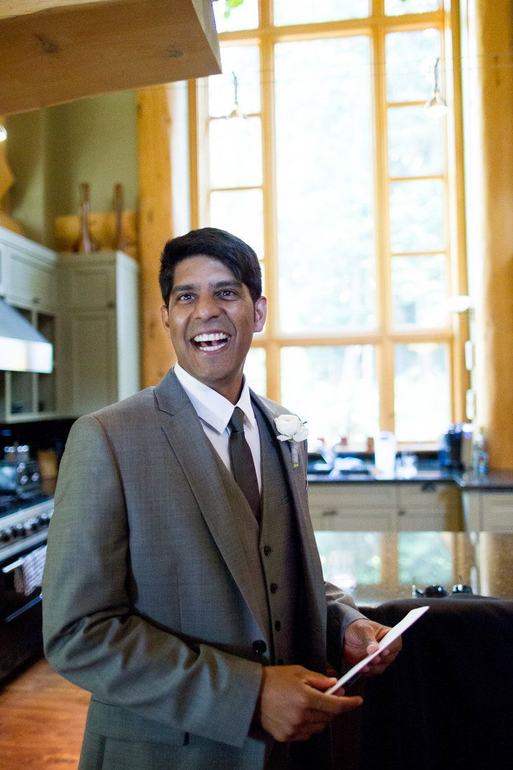 Person in grey suit with boutonniere smiles while holding documents in sunny room.