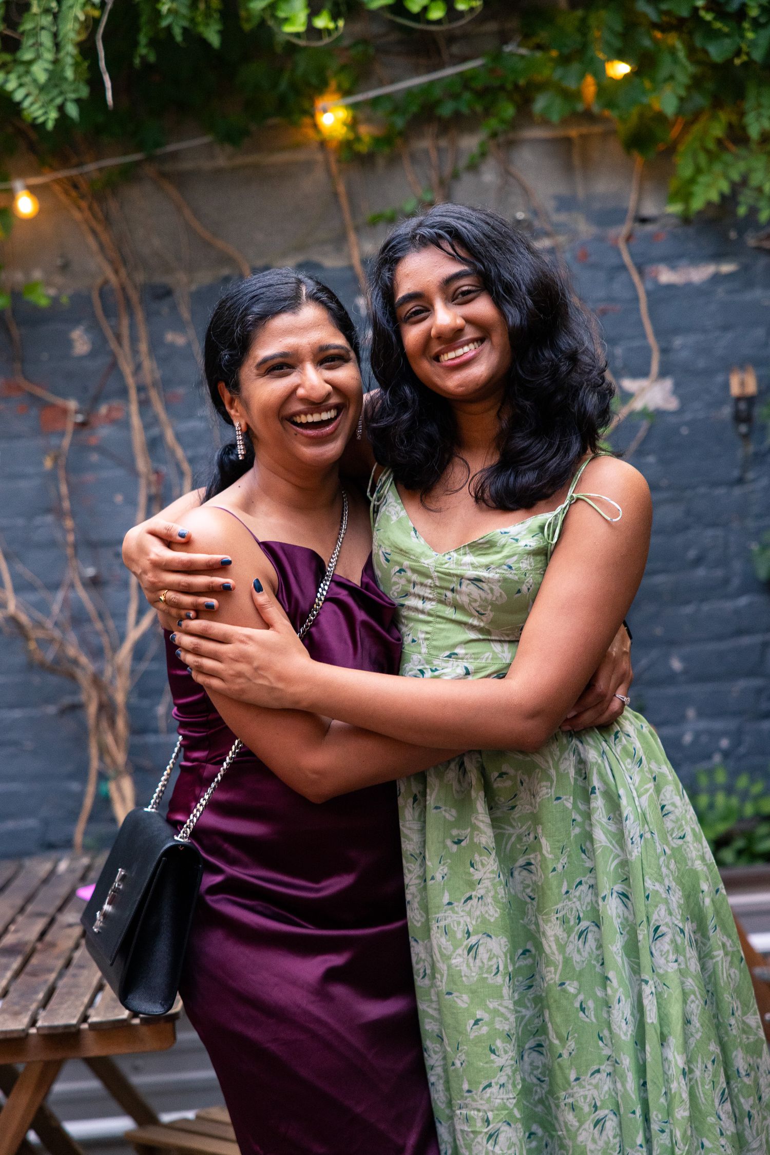 Two women in formal dresses embracing and laughing at an outdoor evening event.