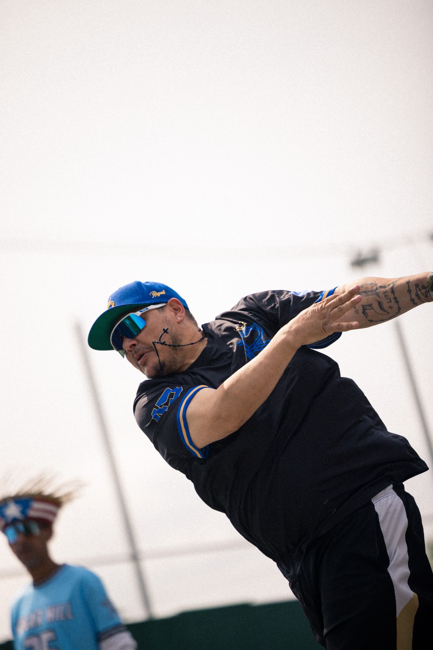 A person wearing black throws a flying disc during a disc golf game against a bright overcast sky.