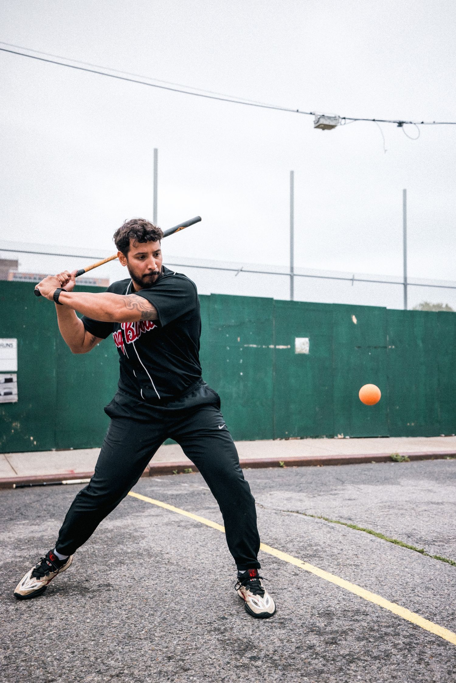 A sequence showing a person in black clothing playing stickball or baseball on a street court.