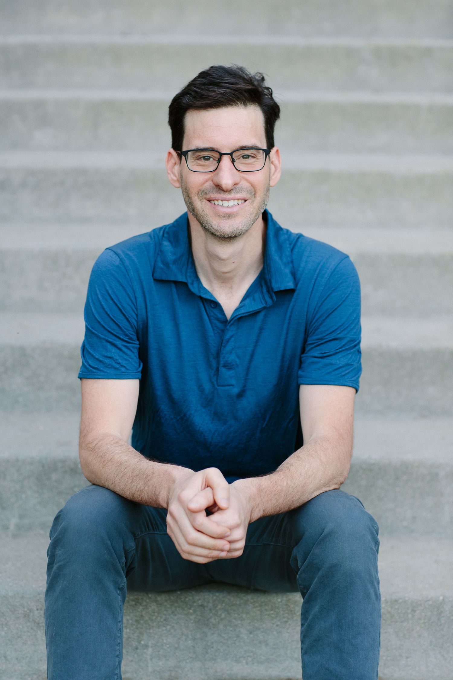 Professional portrait of person in blue polo sitting on concrete steps.