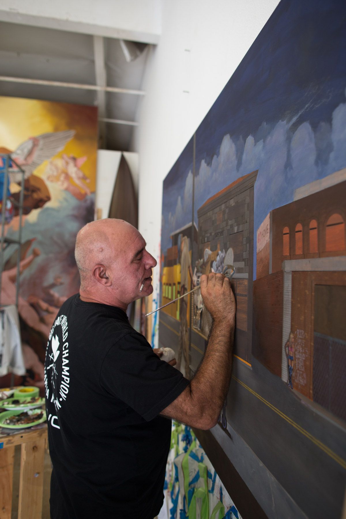 Artist painting a detailed mural on a wall showing buildings and streetscapes.