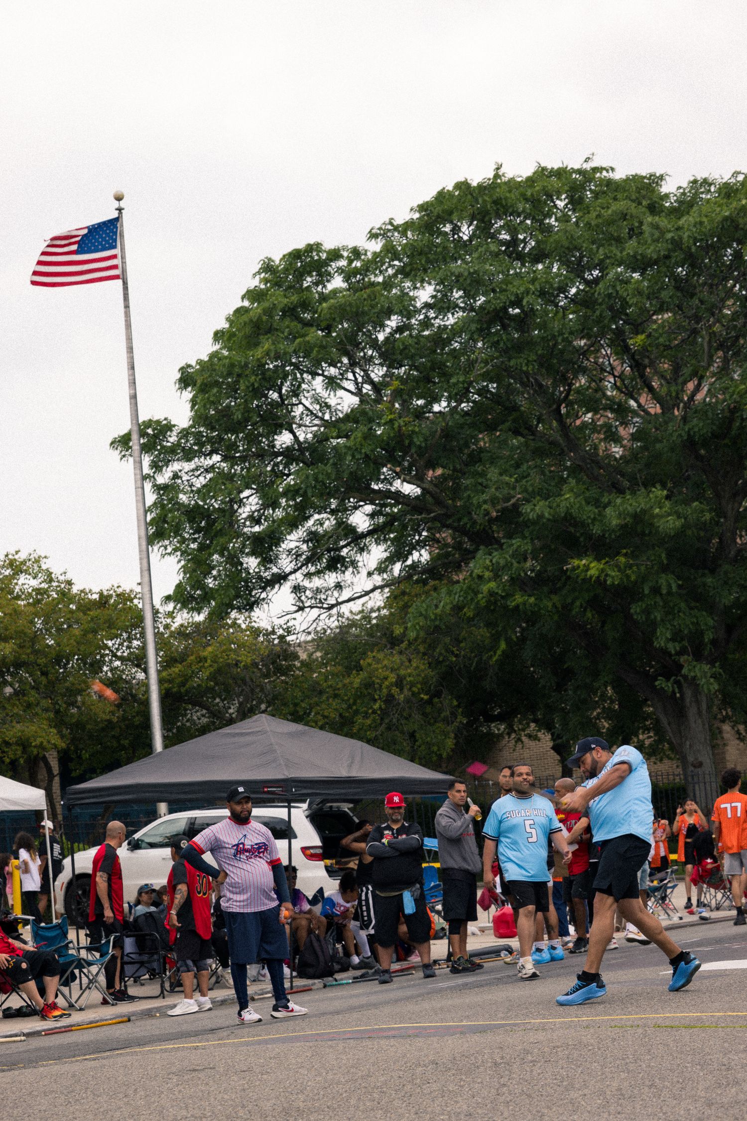 Long line of people waiting outside with tents and American flags at an outdoor event.