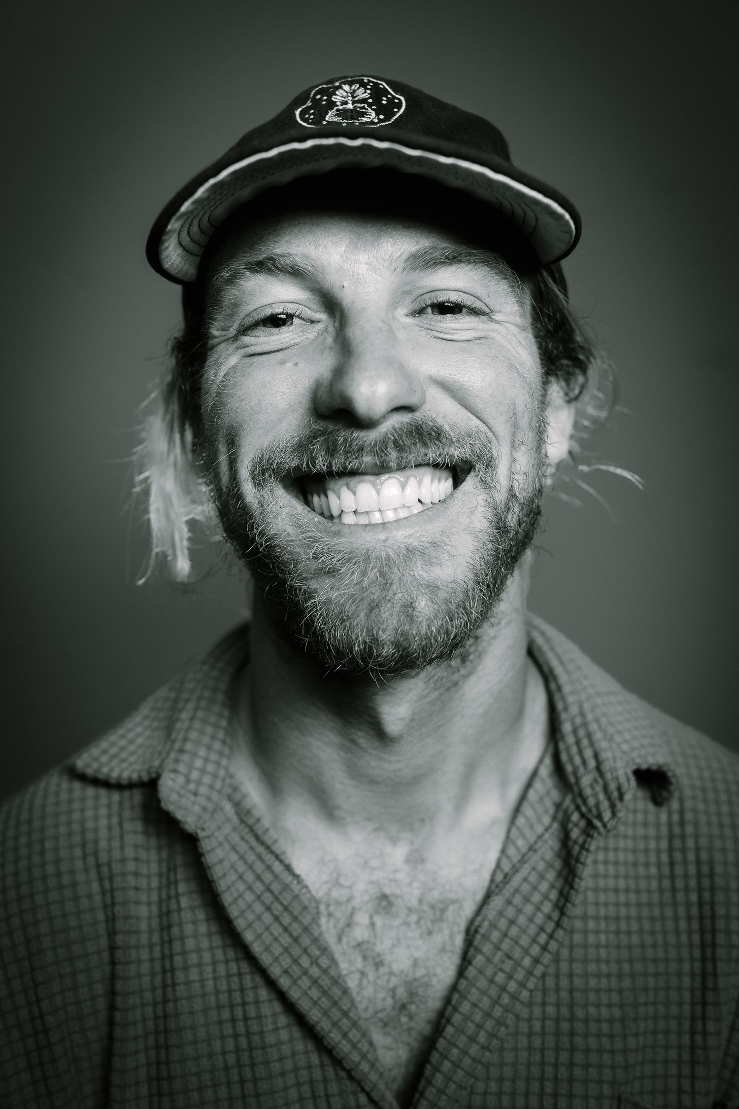 Portrait of a cheerful bearded man in a baseball cap and plaid shirt.