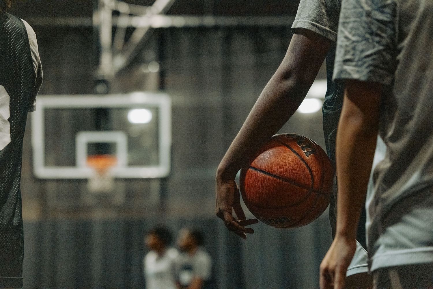Athletes warming up with basketballs in a dimly lit indoor court.