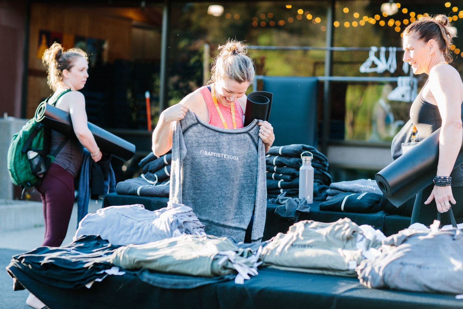 People sort through clothing and equipment laid out on dark mats in a bright indoor space.
