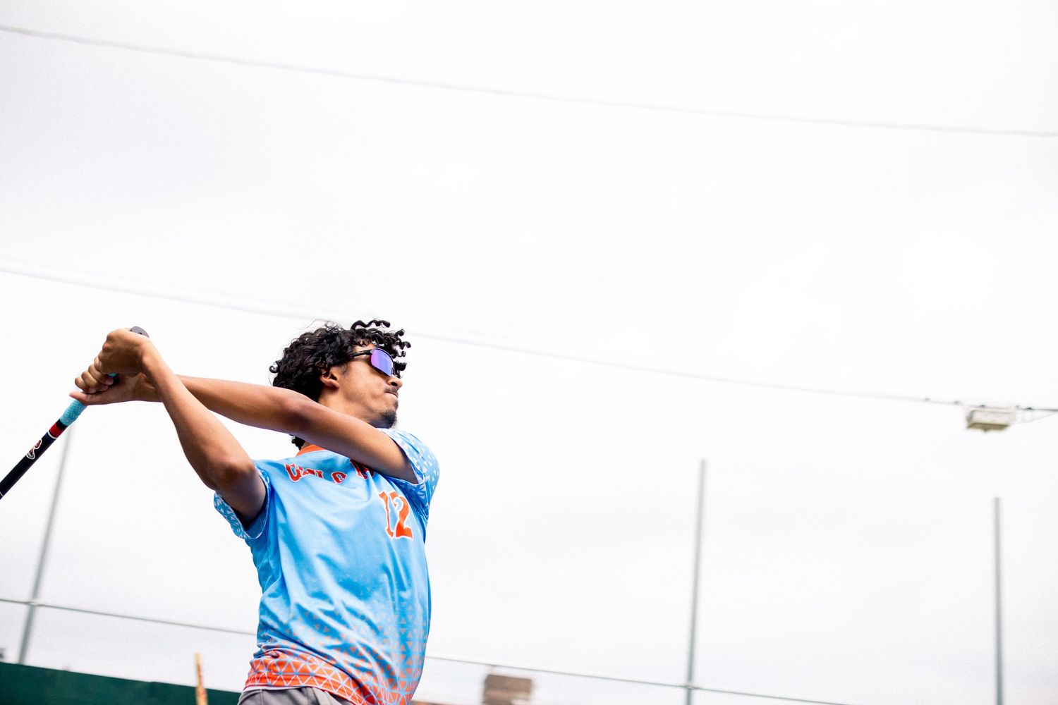 Athlete in light blue jersey taking a powerful swing on an outdoor sports field.