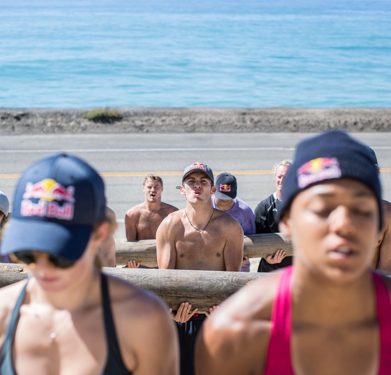 A group of athletes in workout gear training outdoors near the ocean on a sunny day.