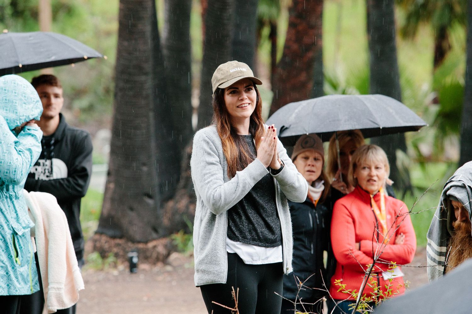 Crowd of people with umbrellas gathered outdoors on a rainy day in a park or wooded area.