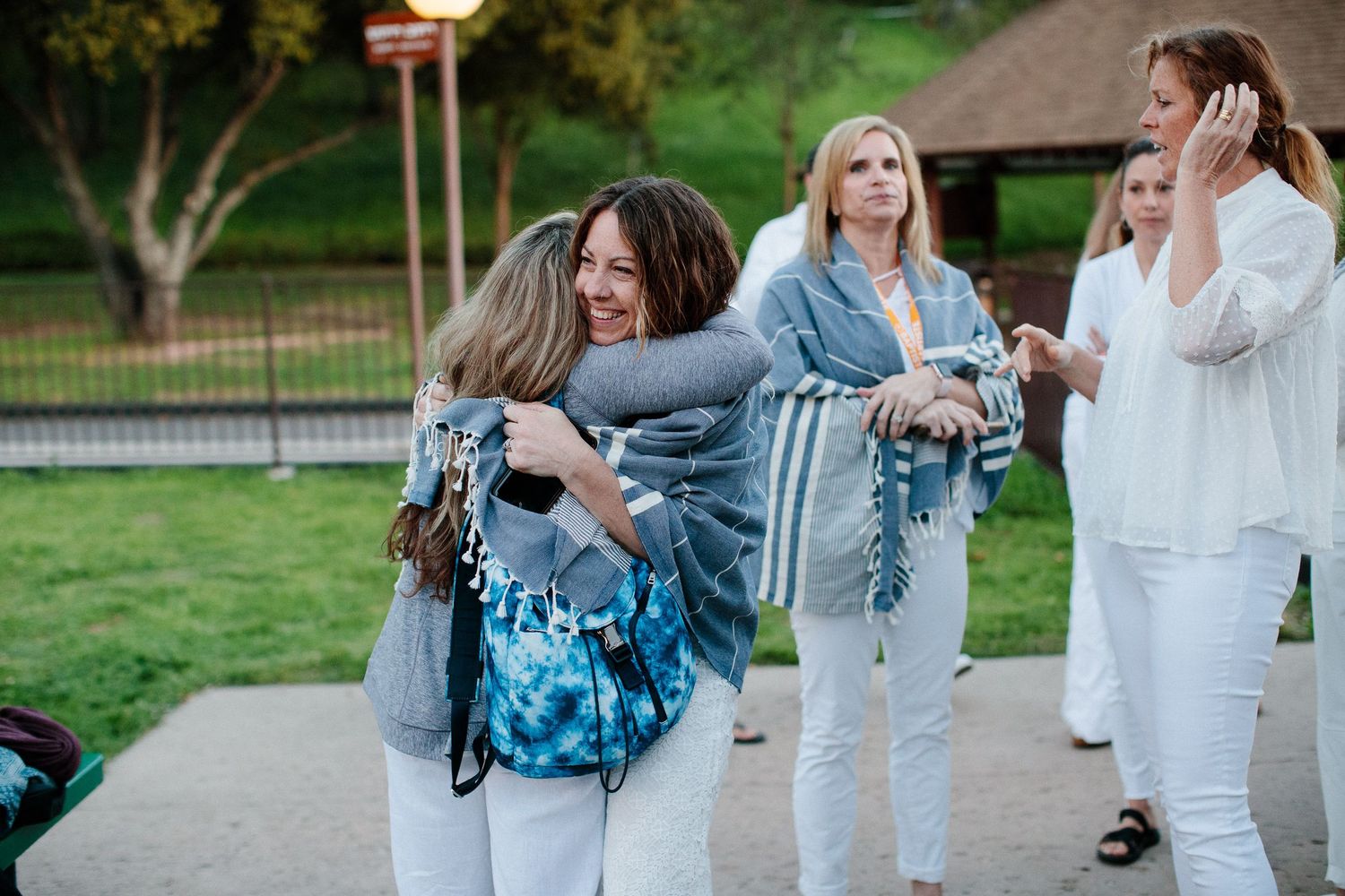 Group gathering outdoors wearing light colored clothing in a park setting.