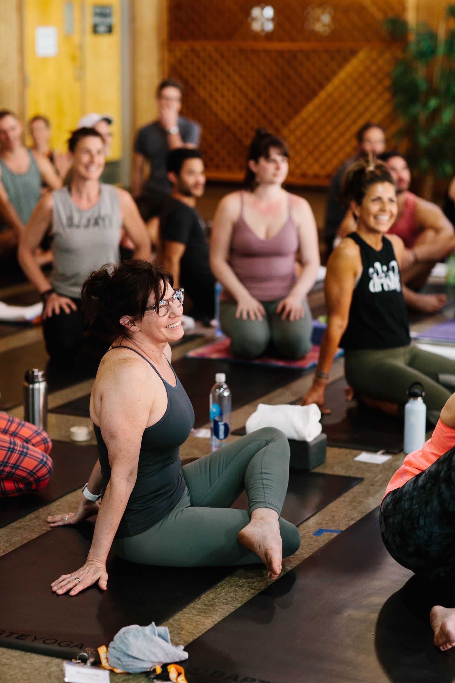 Yoga students practicing poses in a warm-lit studio with wooden lattice walls.