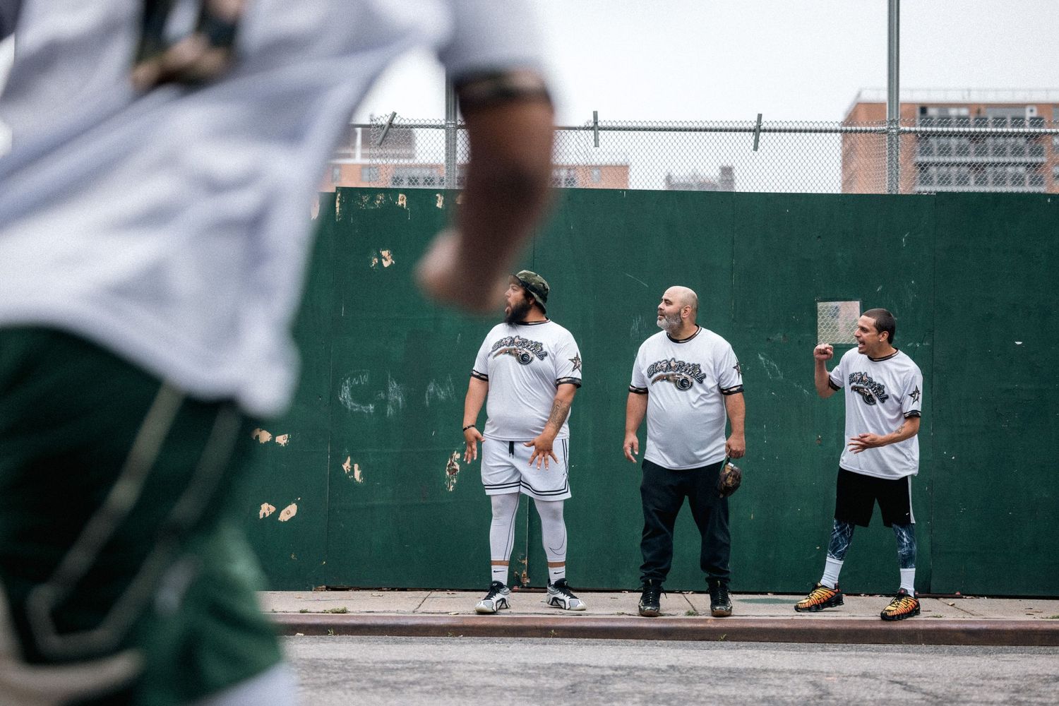 Baseball players watching a game unfold from behind a fence at the field.