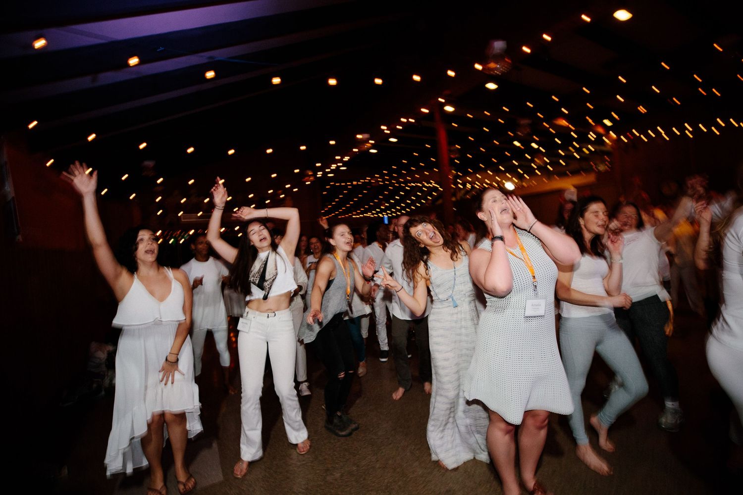 Wedding reception guests dancing under twinkling lights in a dark venue with a festive atmosphere.