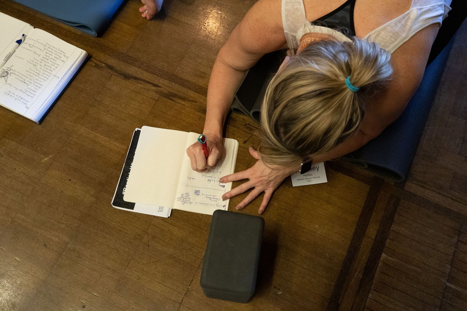 Several hands writing on papers spread across a dark wooden table surface.
