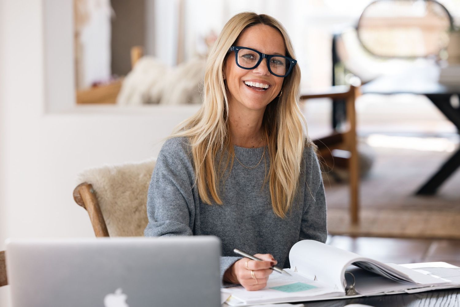 Person writing and studying with books and papers on desk in bright room.