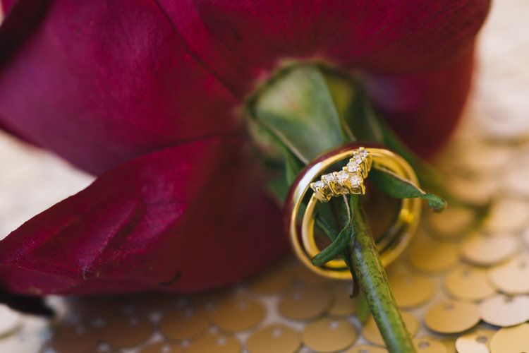 Wedding rings arranged artistically with a deep red rose on a metallic surface with decorative details.
