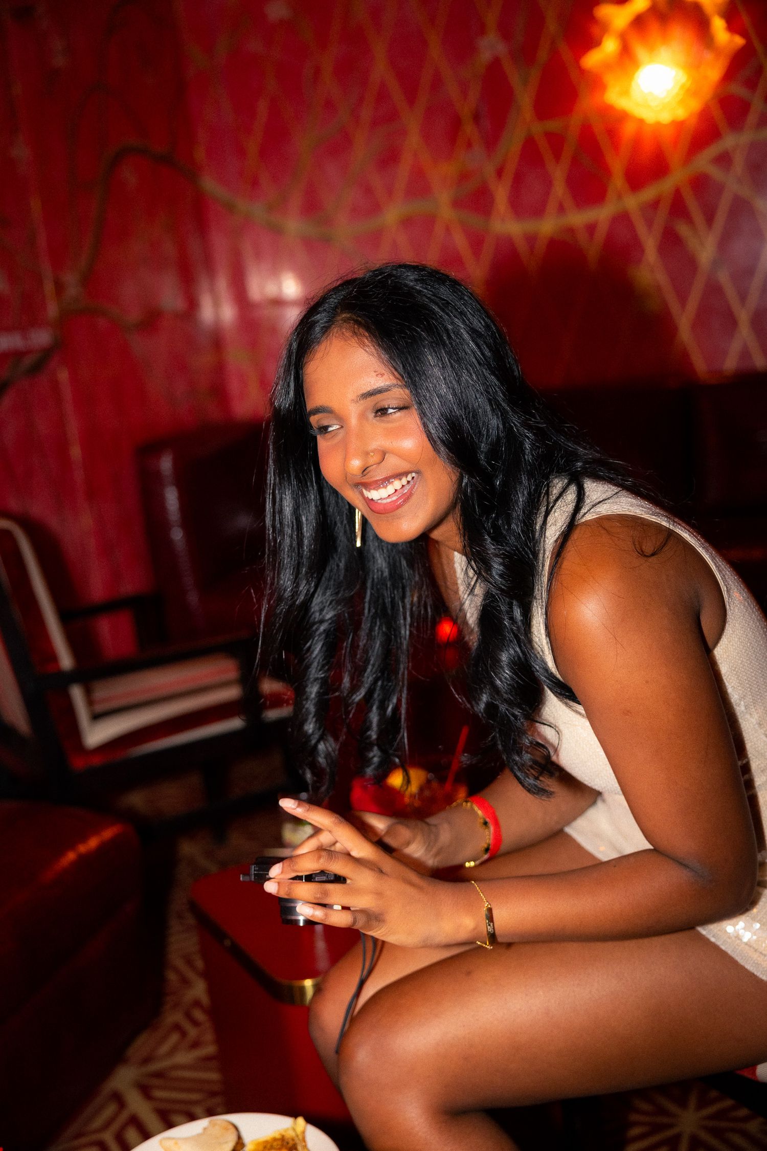 Partygoer in white dress relaxing on red seating at a nighttime event.