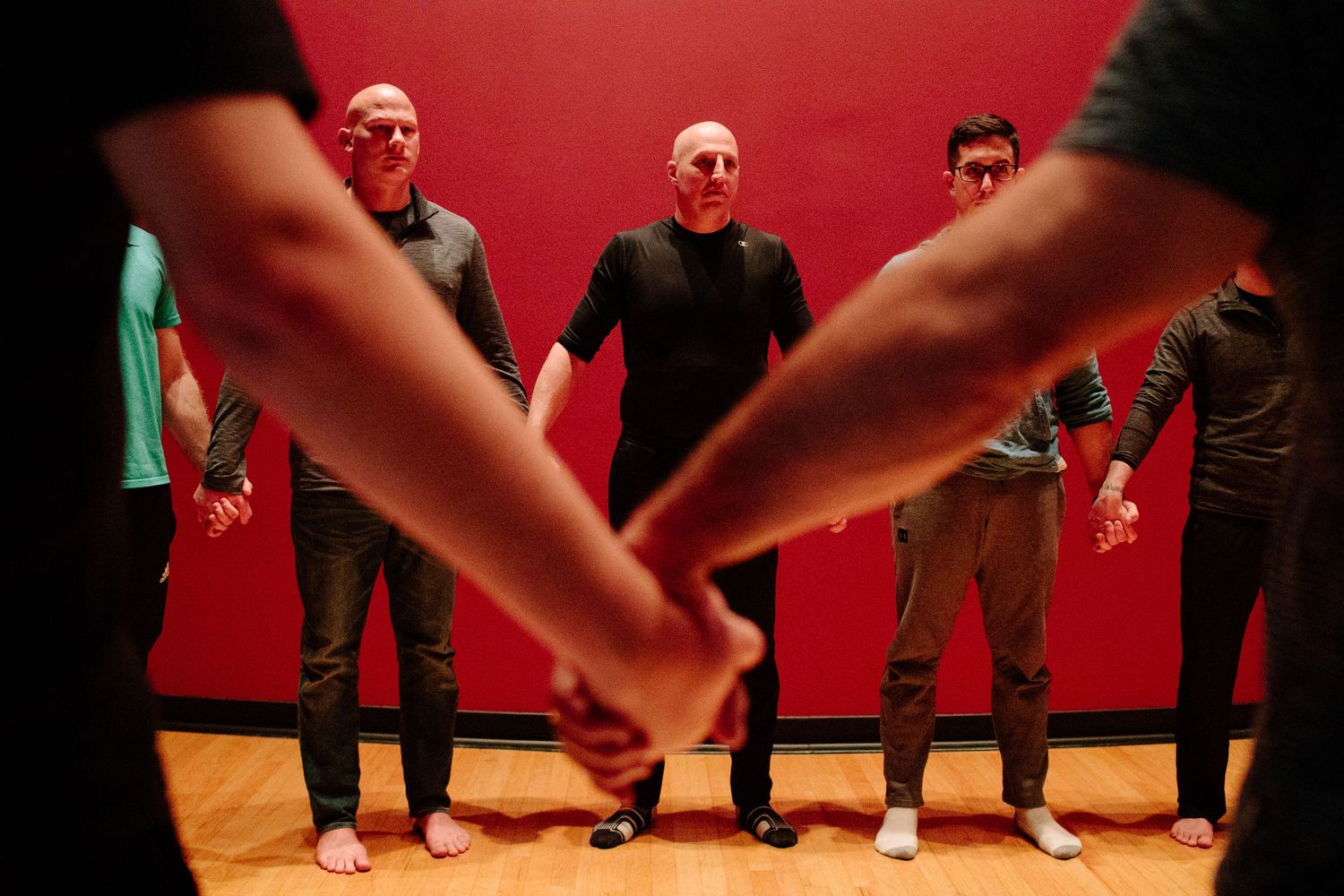 Group of people practicing movement exercises in a studio with red walls and wooden floor.