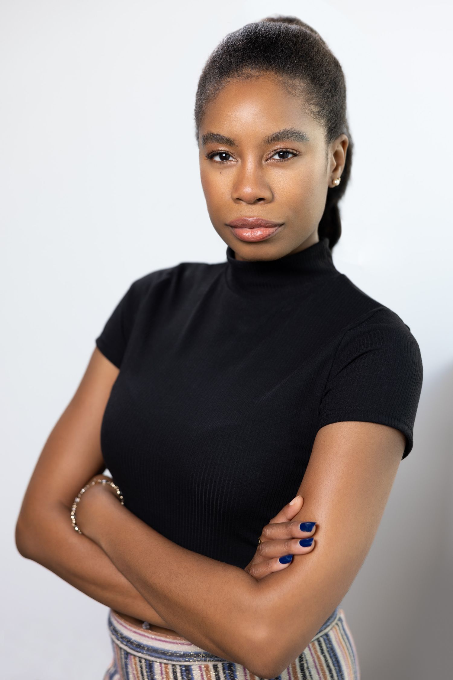Studio portrait of a person in a black turtleneck with crossed arms against white background.