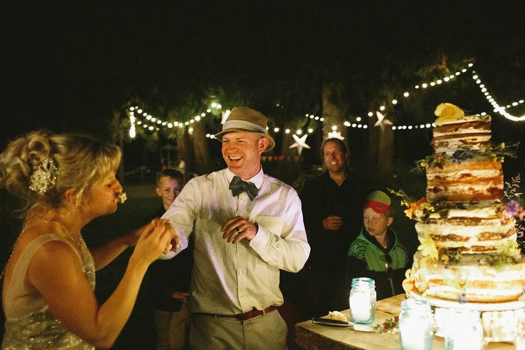 Evening wedding reception scene with dancing and string lights near a decorated cake.