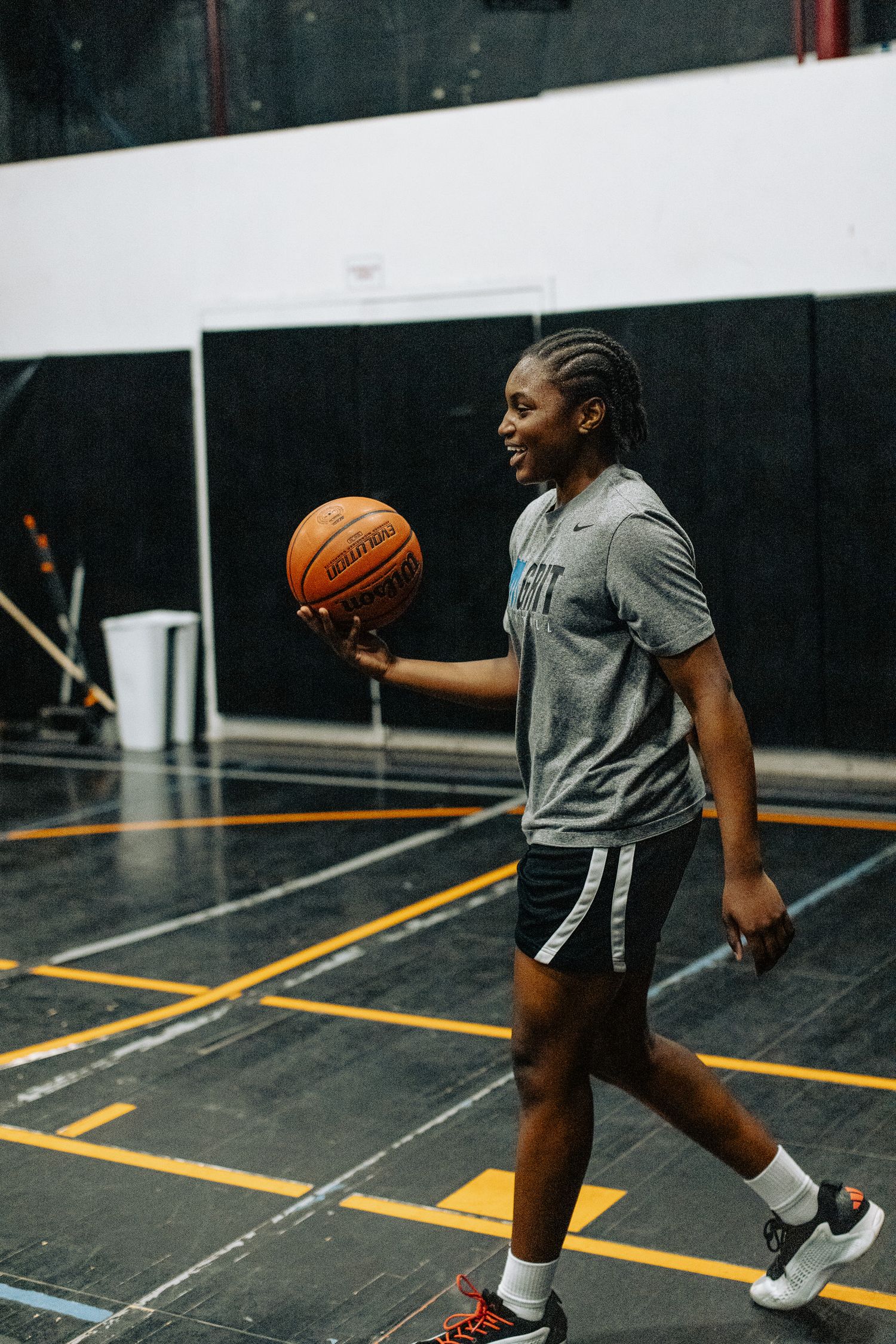 Basketball player in grey t-shirt and black shorts dribbles on indoor court during practice session.