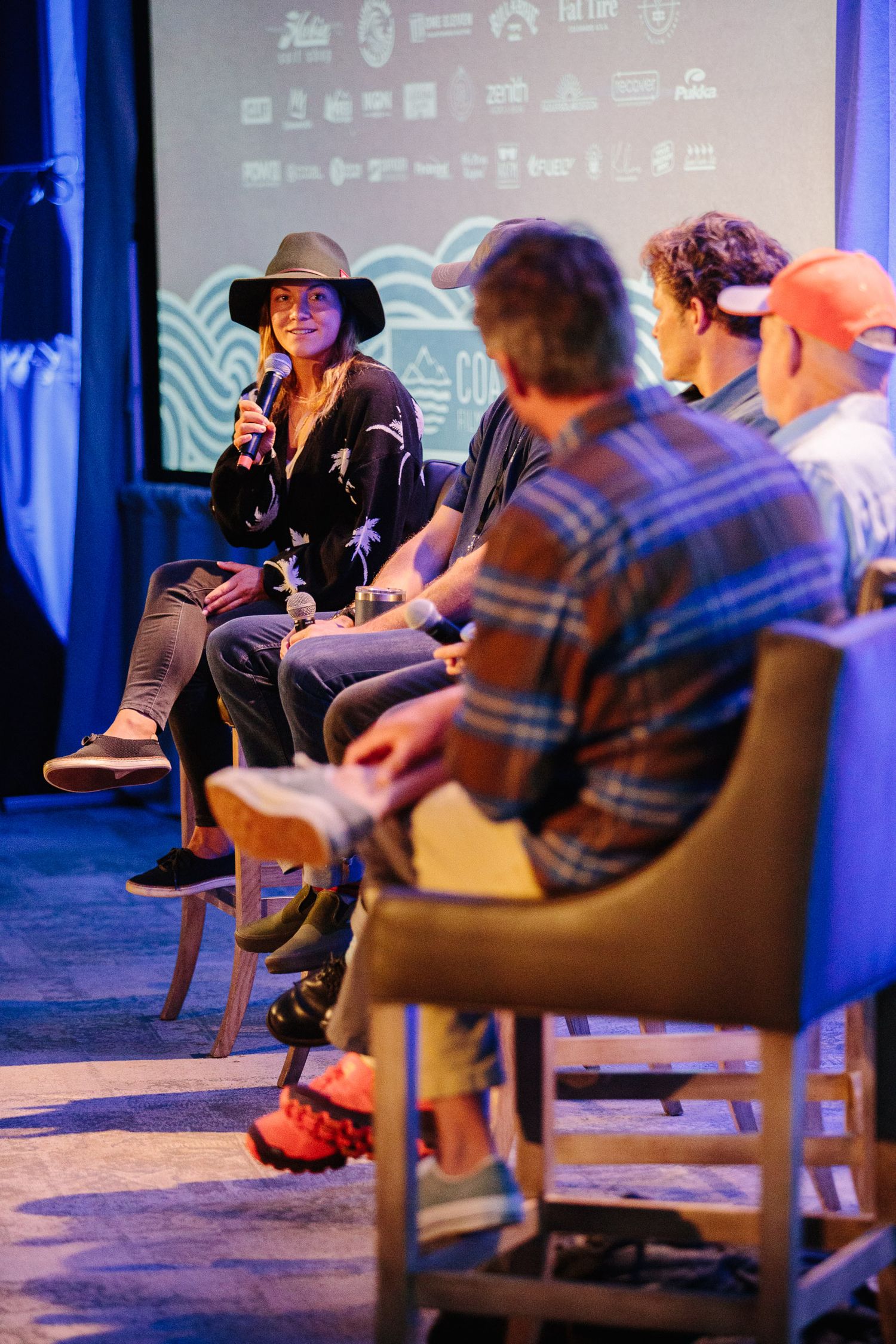 Conference panel discussion setup with speakers seated on stage under blue lighting.
