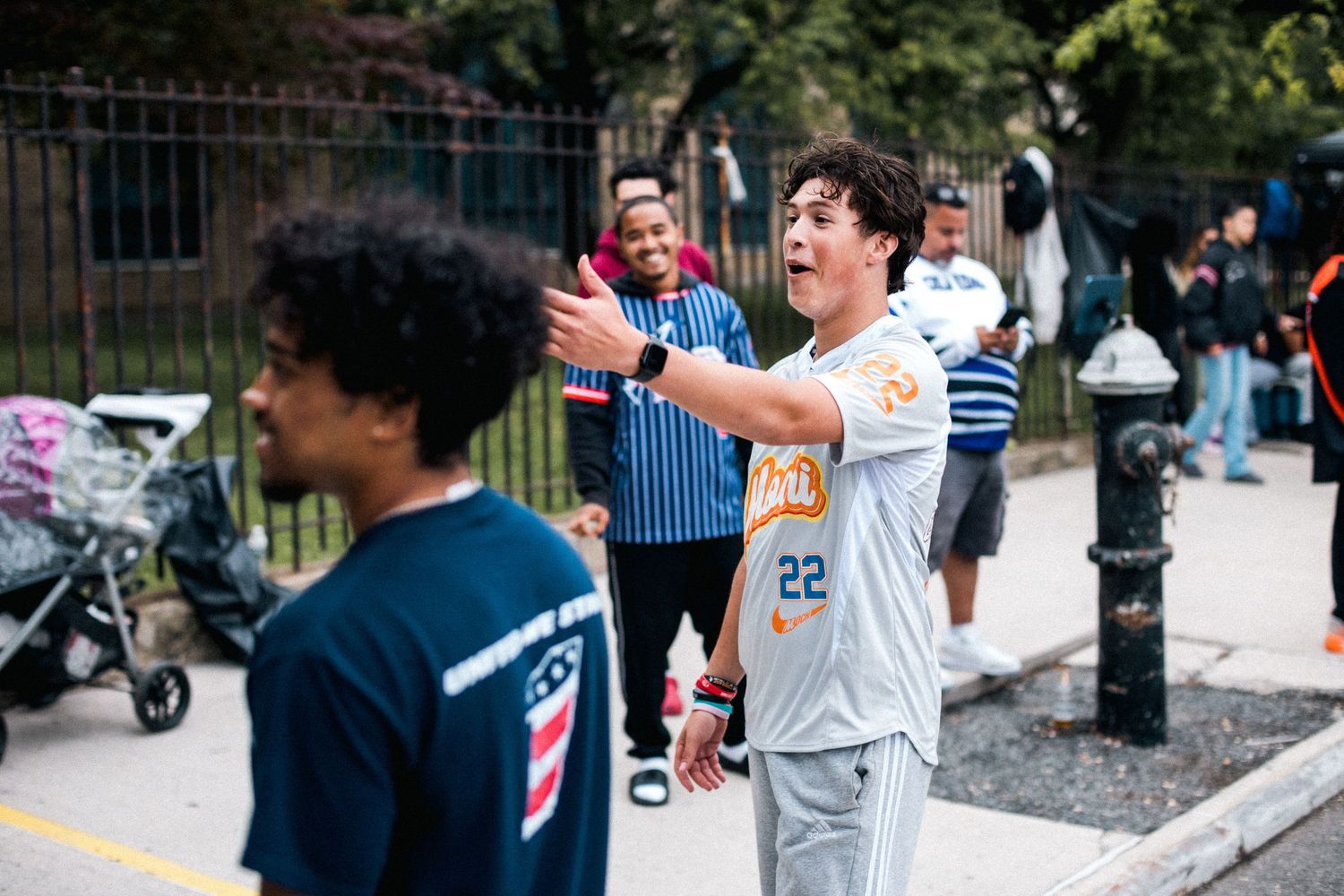 People playing sports and socializing at an outdoor community event near a fence.