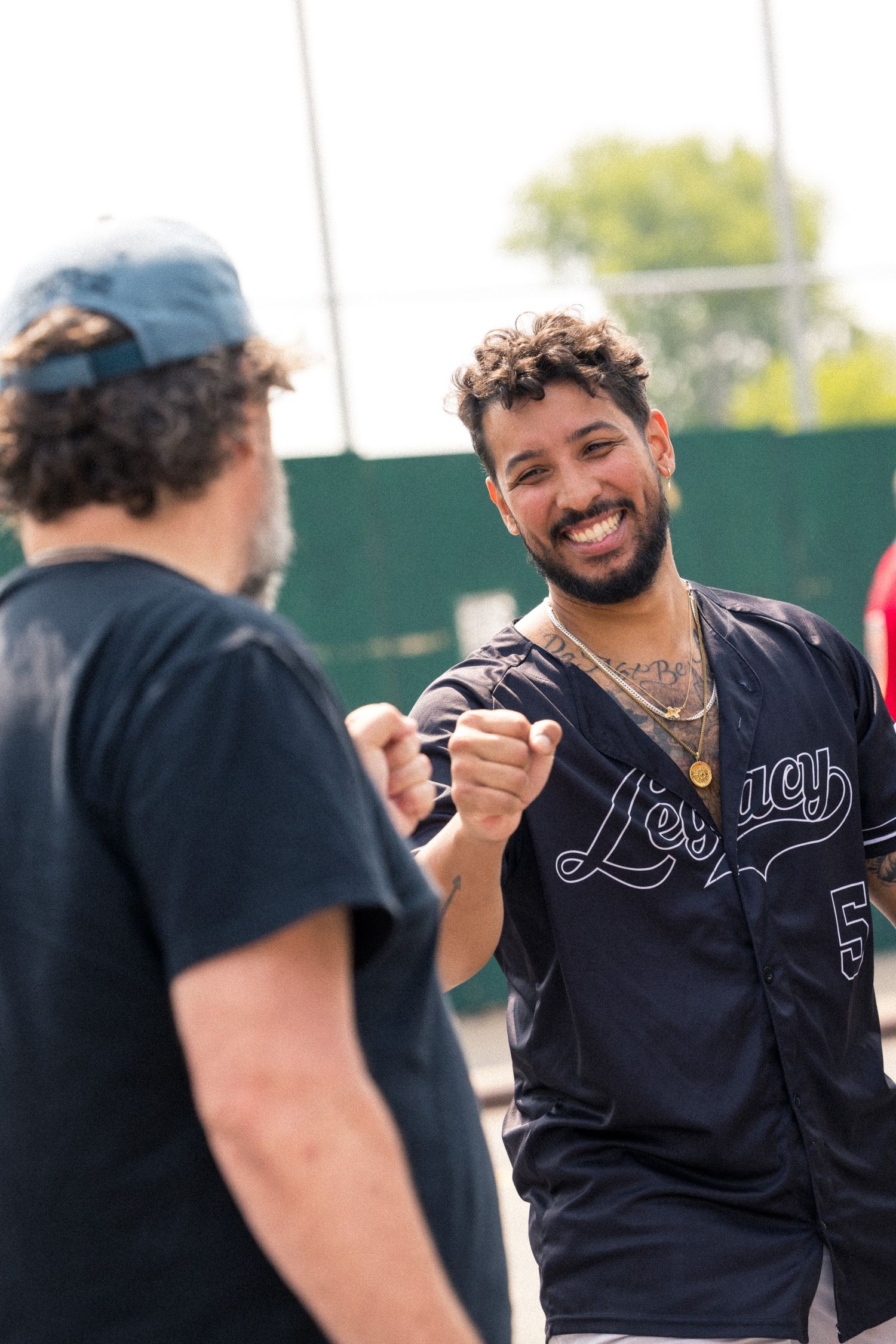 Two teammates share a friendly fist bump while wearing baseball uniforms during an outdoor game.