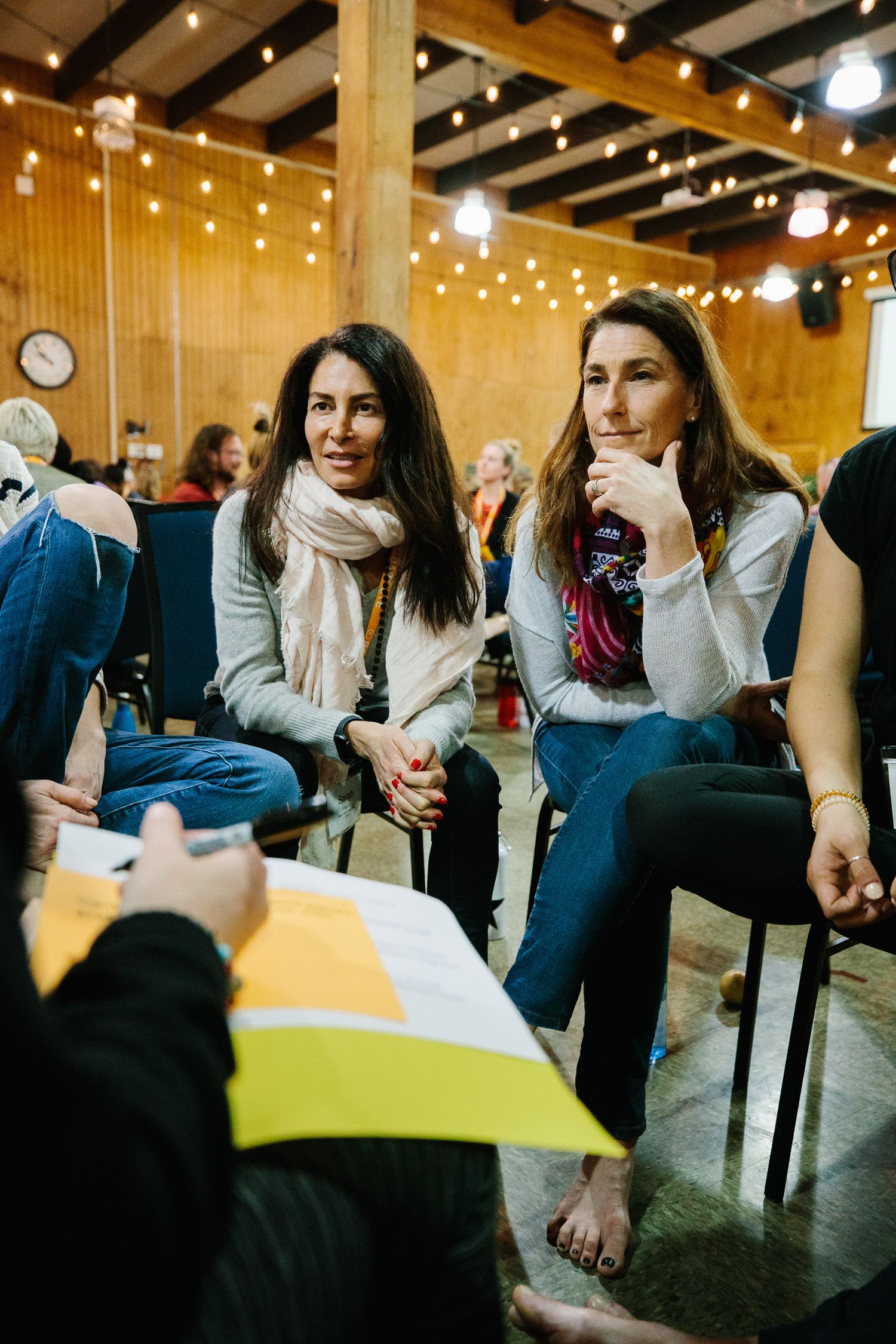 People sitting barefoot in chairs having a discussion in a warmly lit room with string lights overhead.