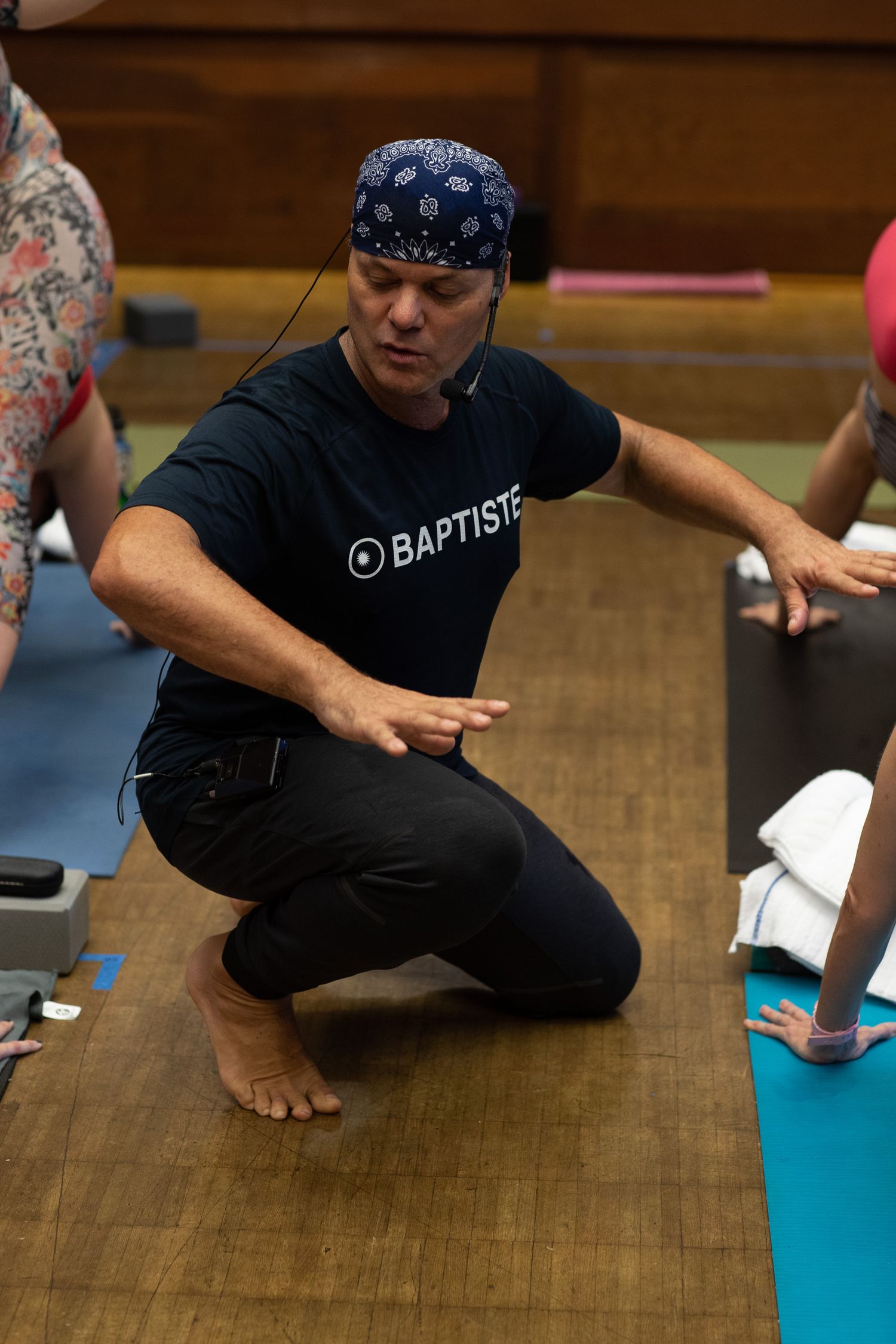Person in black clothing sitting on wooden floor with turquoise yoga mat.