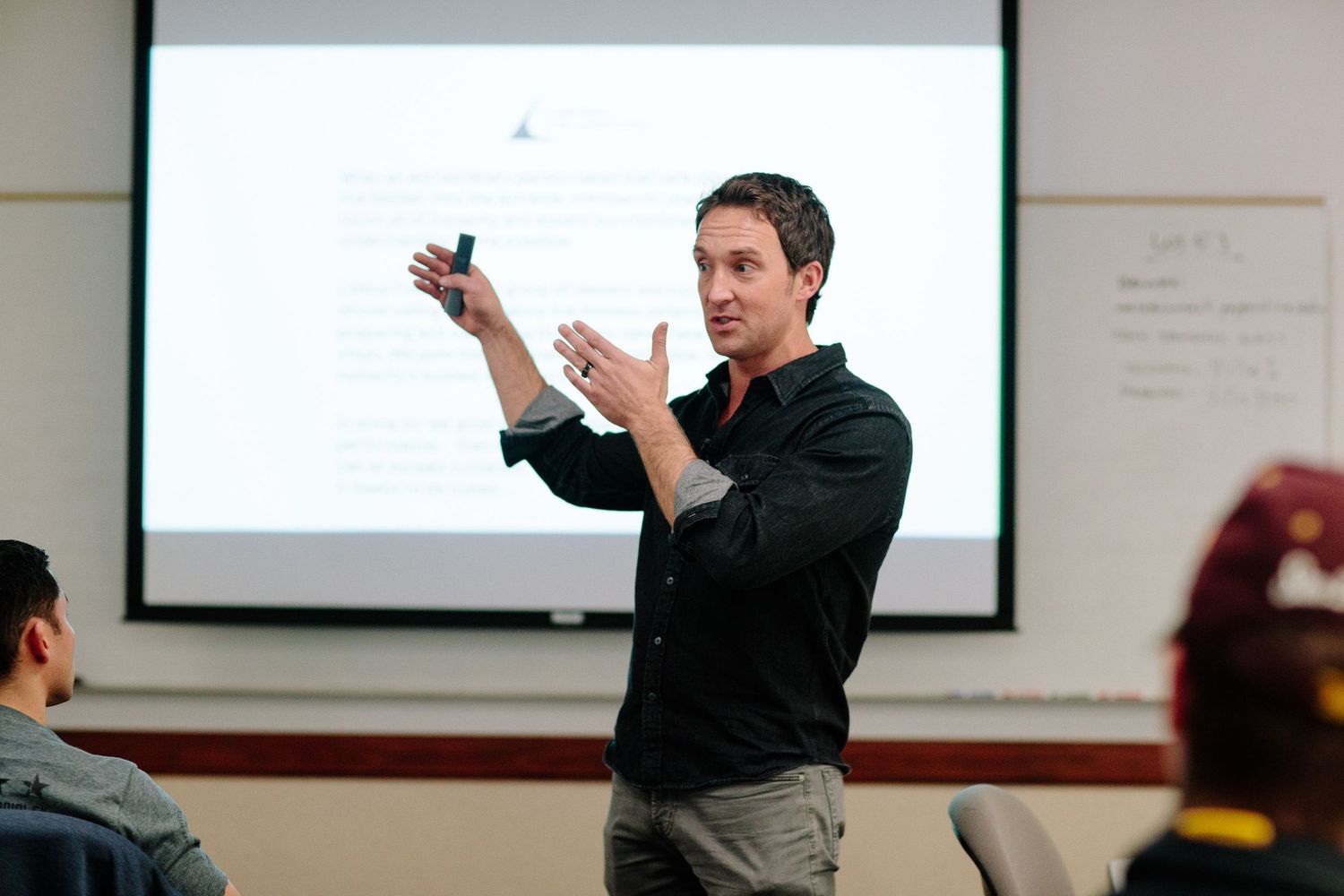 A presenter gesturing while giving a presentation in front of a projection screen.